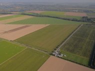 Weitläufige Felder mit einem kleinen Gebäudekomplex im Zentrum einer L-förmigen Struktur in der Landschaft.