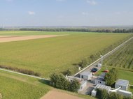 Fields stretch to the horizon, with several buildings, two long tunnels at ground level, and a parking lot in the foreground, surrounded by green spaces.