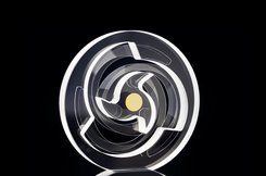 Transparent circular object with intricate internal geometric patterns, including a central yellow dot, set against a dark background.