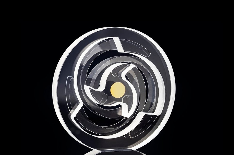 Transparent circular object with intricate internal geometric patterns, including a central yellow dot, set against a dark background.